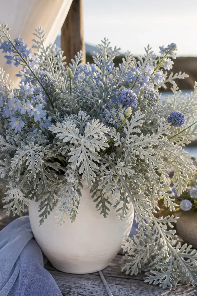 Dusty miller foliage with pale blue ribbon and ivory candles on a beach table