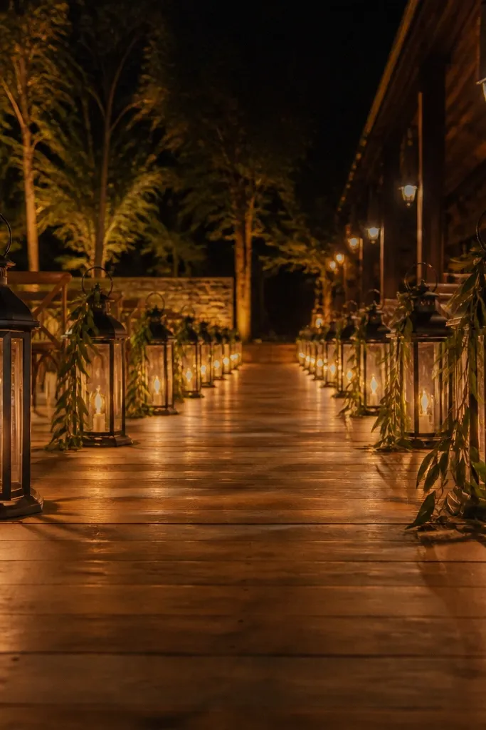 Dark iron lanterns lining a wedding aisle with warm lights and greenery