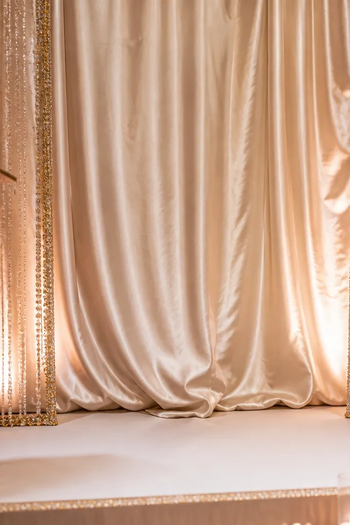 Champagne silk backdrop with a beaded fringe border around the frame