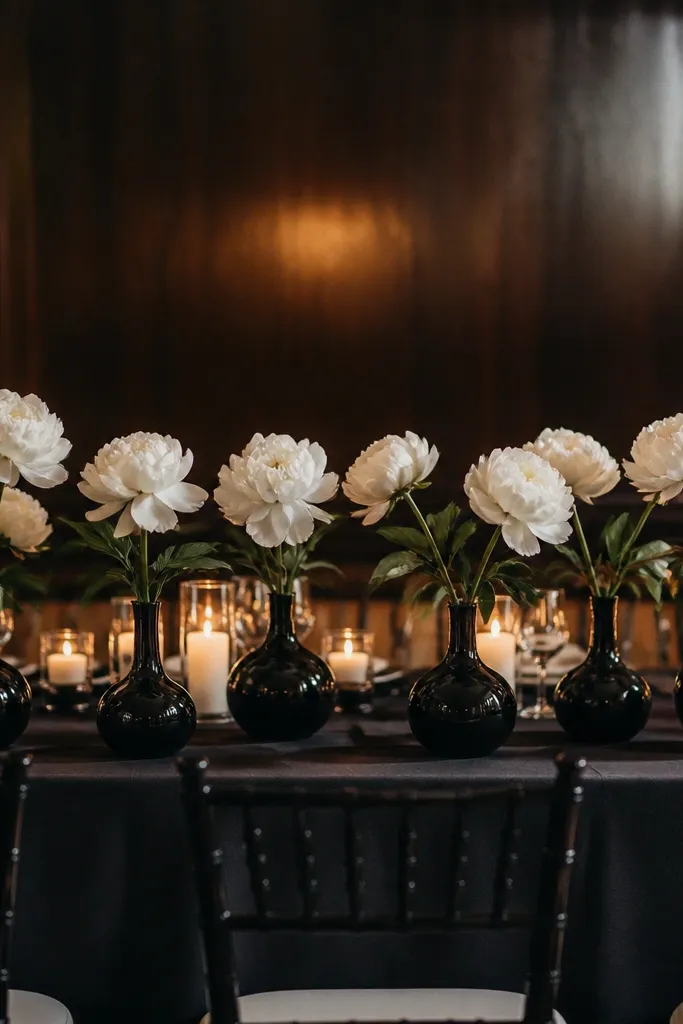 Black bud vases spaced along a runner with faux white peony blooms