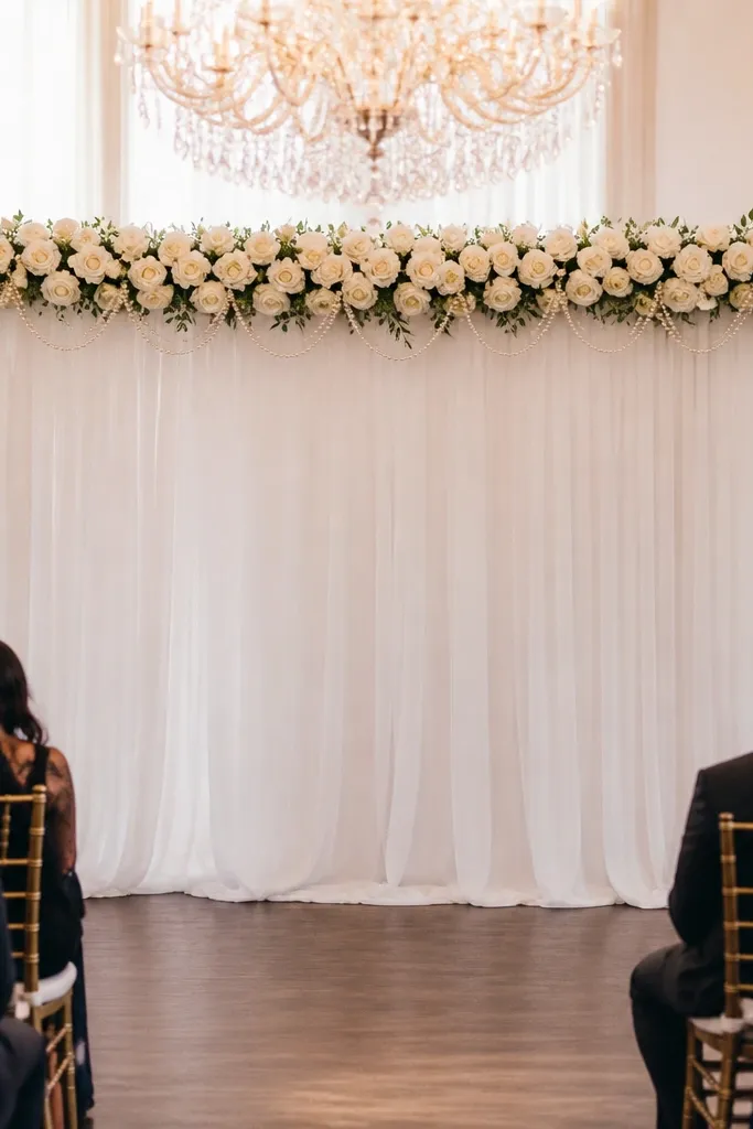White rose garland with pearl accents draped across the top of a stage frame