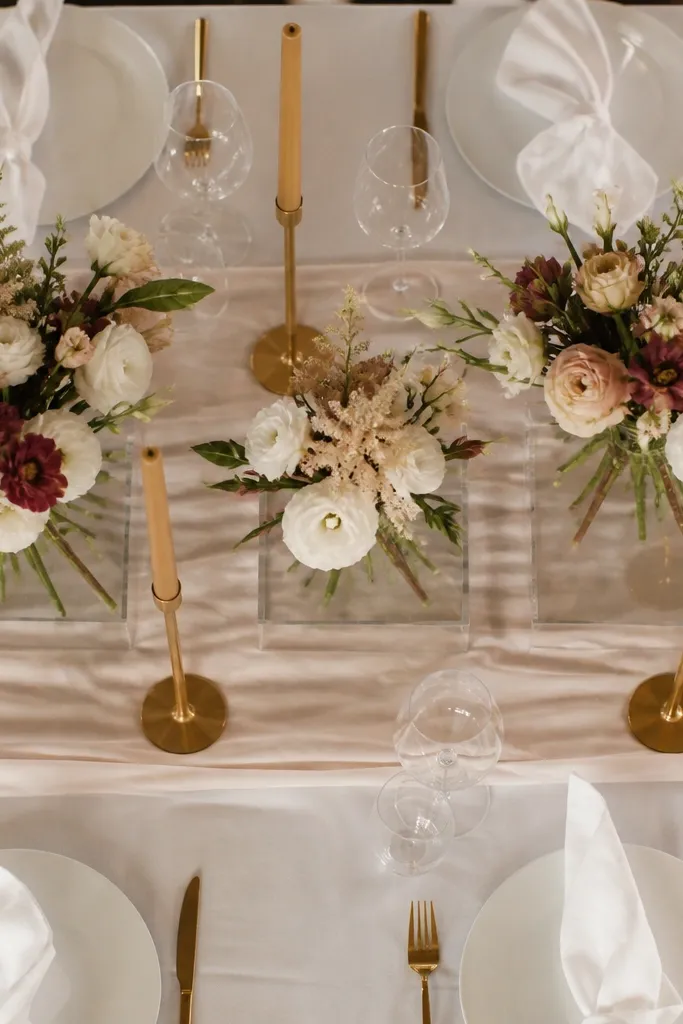 White floral runner on a table with clear acrylic risers and gold candles