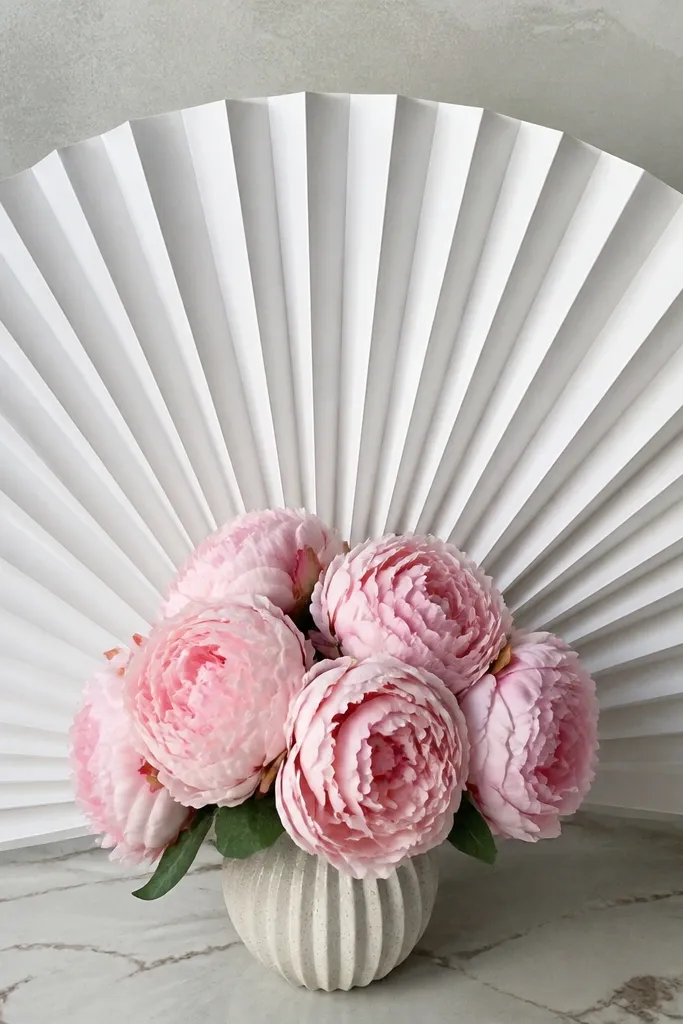 Folded white paper fan backdrop with a small pink flower arrangement in front