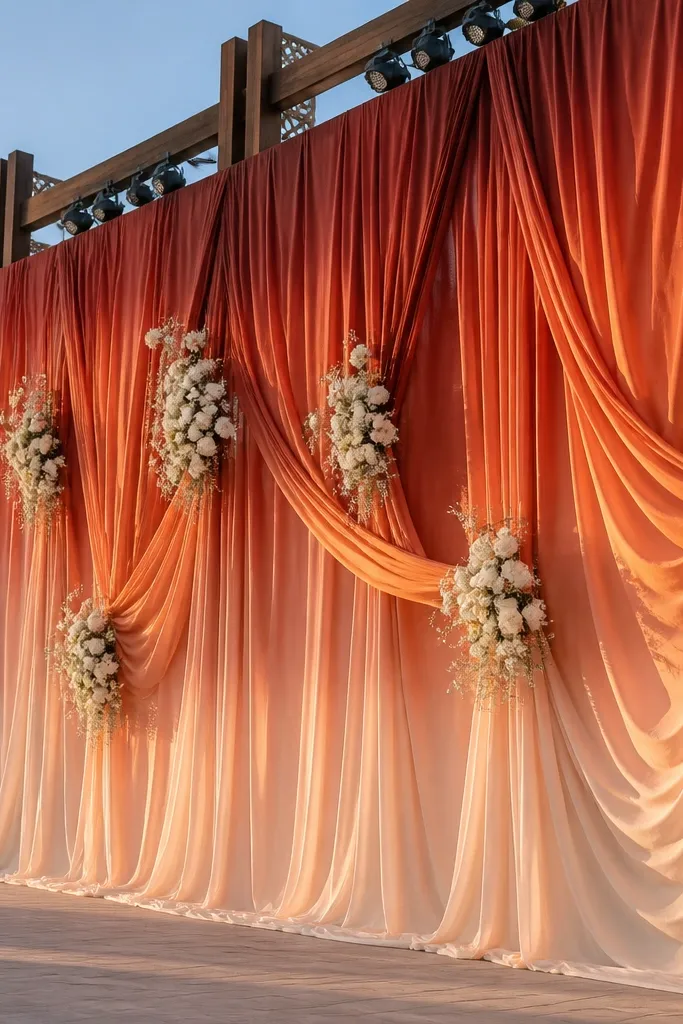 Terracotta ombre fabric drapes behind stage with white floral sprays