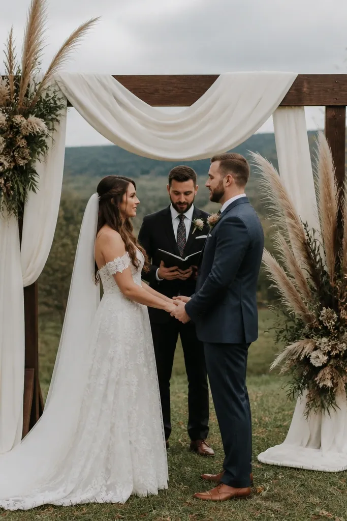 Rustic arch draped in cream linen with tall feathery plumes and dark greenery