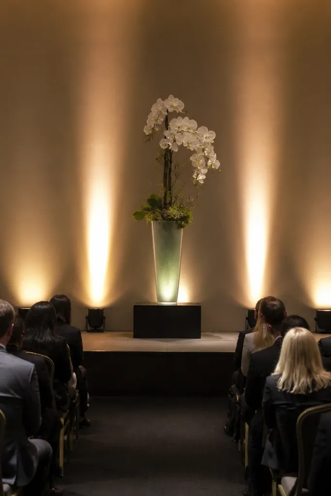 Clean stage lit with warm uplights and a single sculptural centerpiece at center