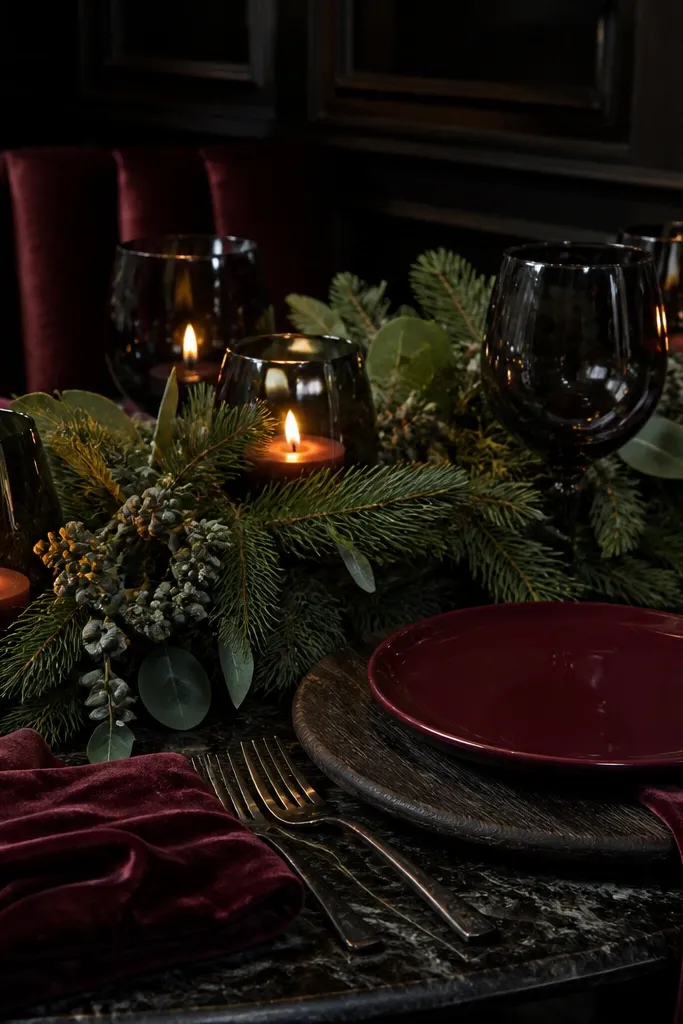 Oxblood napkins, dark green foliage garland, and black glass candle holders on a warm neutral table