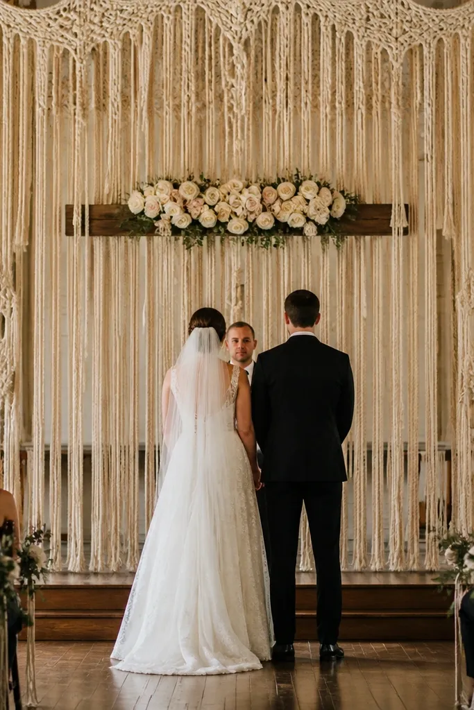 Neutral rose clusters on a macrame fringe curtain wedding stage backdrop
